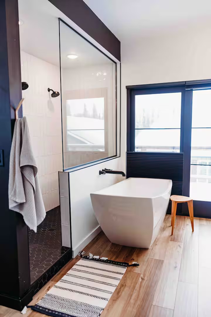 Freestanding tub, black tile, warm wood.